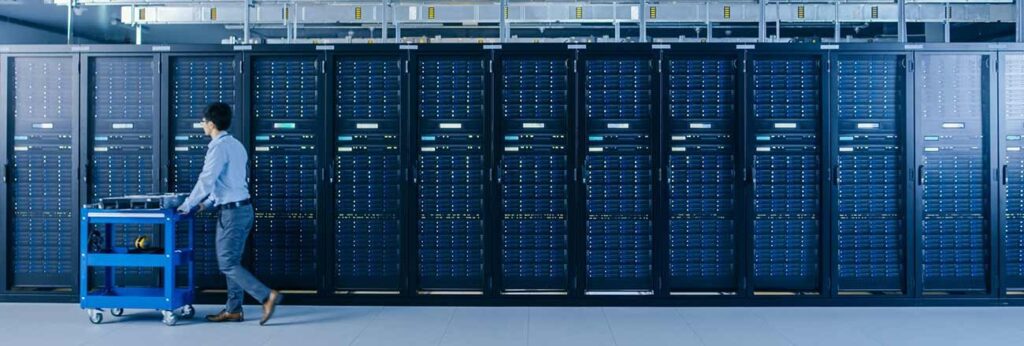 A room full of servers and a man passing beside servers, a perfect image of knowing What is a Dedicated Server